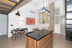 Una cucina moderna con isola centrale, zona pranzo con sedie, illuminazione a sospensione e un'ampia finestra dotata di persiane.
