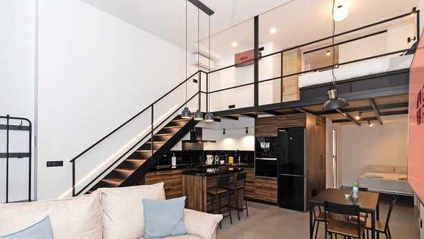 A modern interior with a staircase leading to a loft area, a kitchen with a bar, and a dining area. - GuestReady - Apartment with Mezzanine in Benicalap (Valencia)