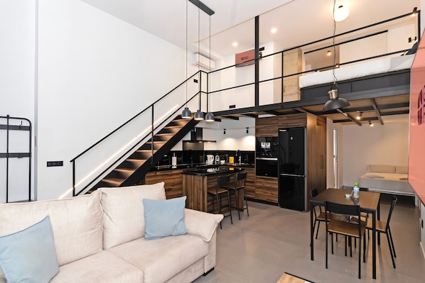 Un interno moderno con una scala che conduce a una zona mansardata, una cucina con un bancone e un'area pranzo.