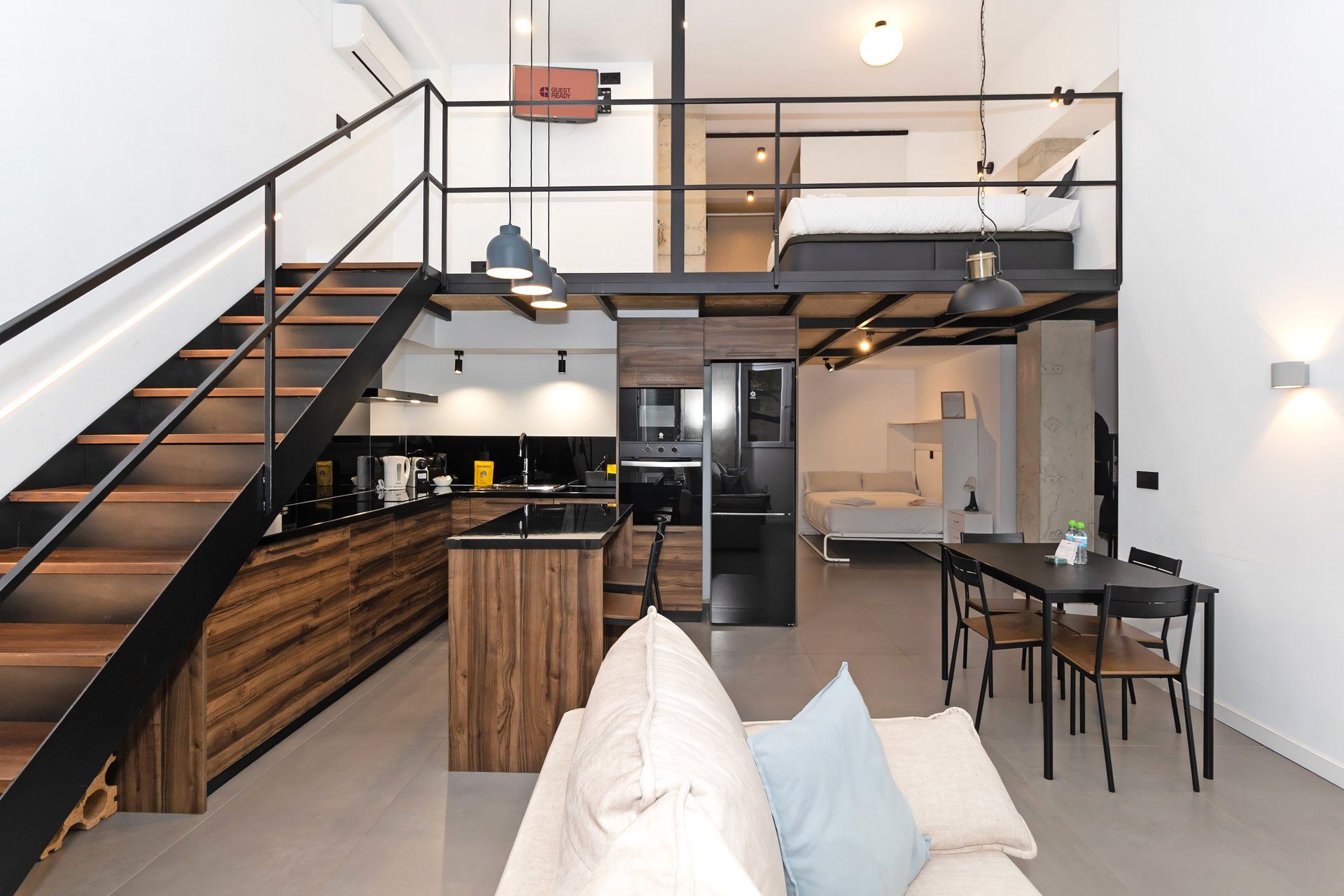 Un interior moderno con una escalera, cocina, comedor y un sofá con cojines.