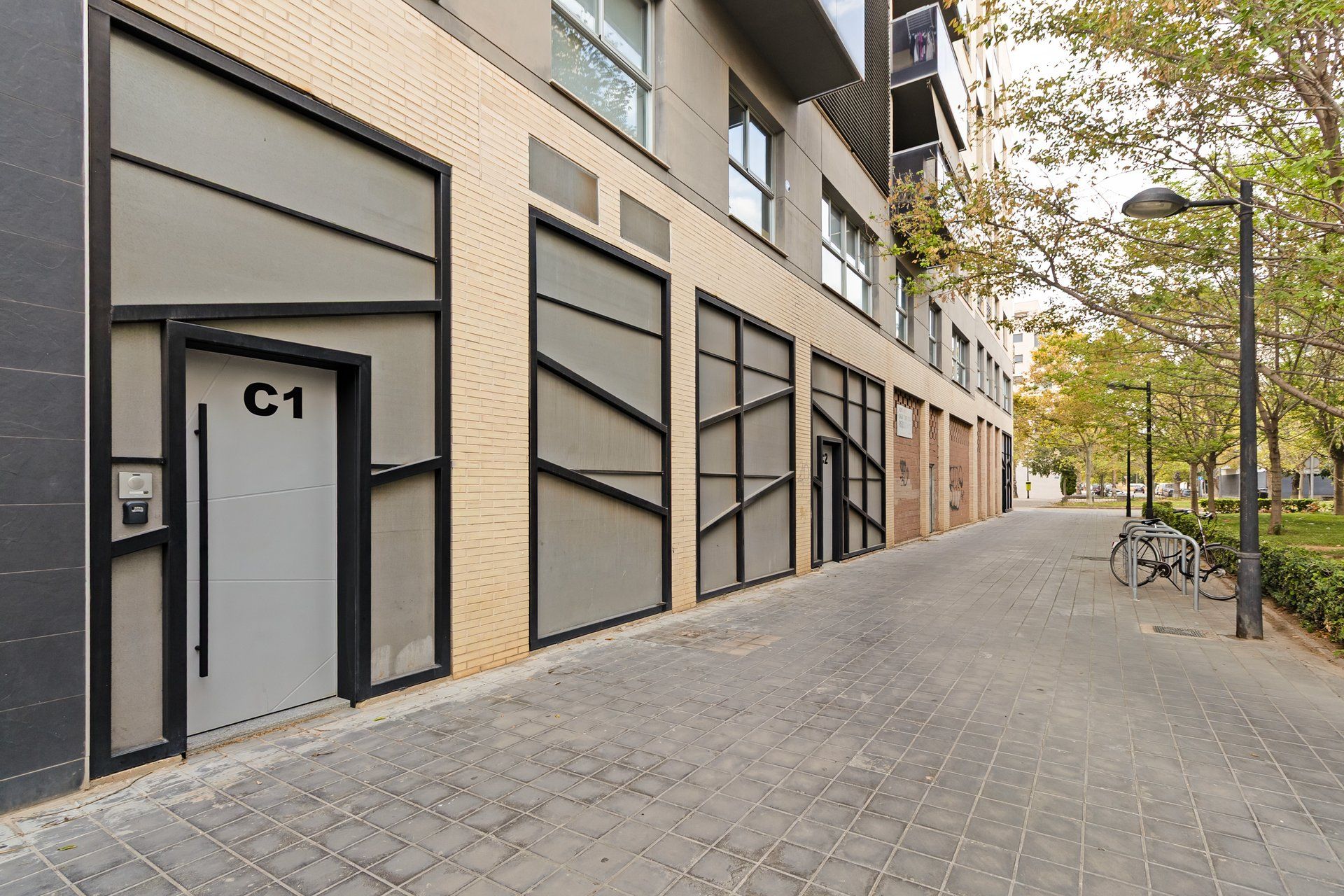 Un edificio moderno con grandes puertas de garaje, un sendero pavimentado y una bicicleta estacionada afuera.