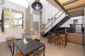 Una cocina moderna con una isla central, una zona de comedor con mesa y sillas, y una escalera que conduce a un nivel superior.