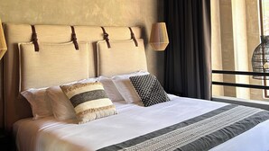 Et hotelværelse med træloft, en stor seng med mange puder, en hængende lampe og udsigt gennem et vindue.