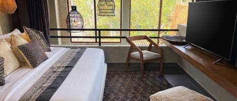 A hotel room with a bed, a television, a chair, and a large window with a view of greenery.