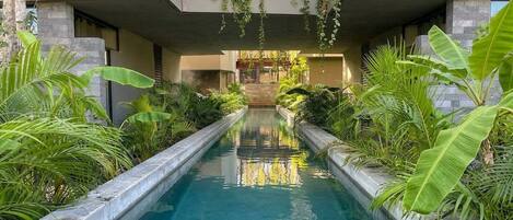 A pool with a stone-lined pathway, surrounded by lush tropical plants.