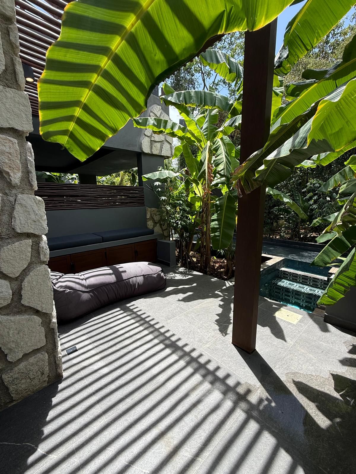 Un mur en pierre, un espace détente avec des coussins et une piscine dont le fond est décoré de motifs géométriques en mosaïque.