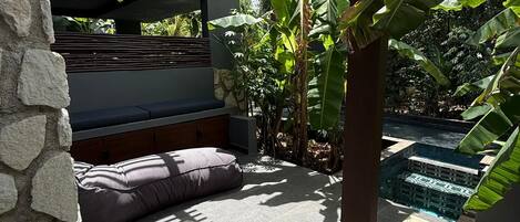 A stone wall, a seating area with cushions, and a pool with a geometric tile pattern.