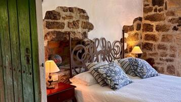 Un dormitorio con pared de piedra, una cama con almohadillas estampadas, una mesita de noche con lámpara y una puerta verde.