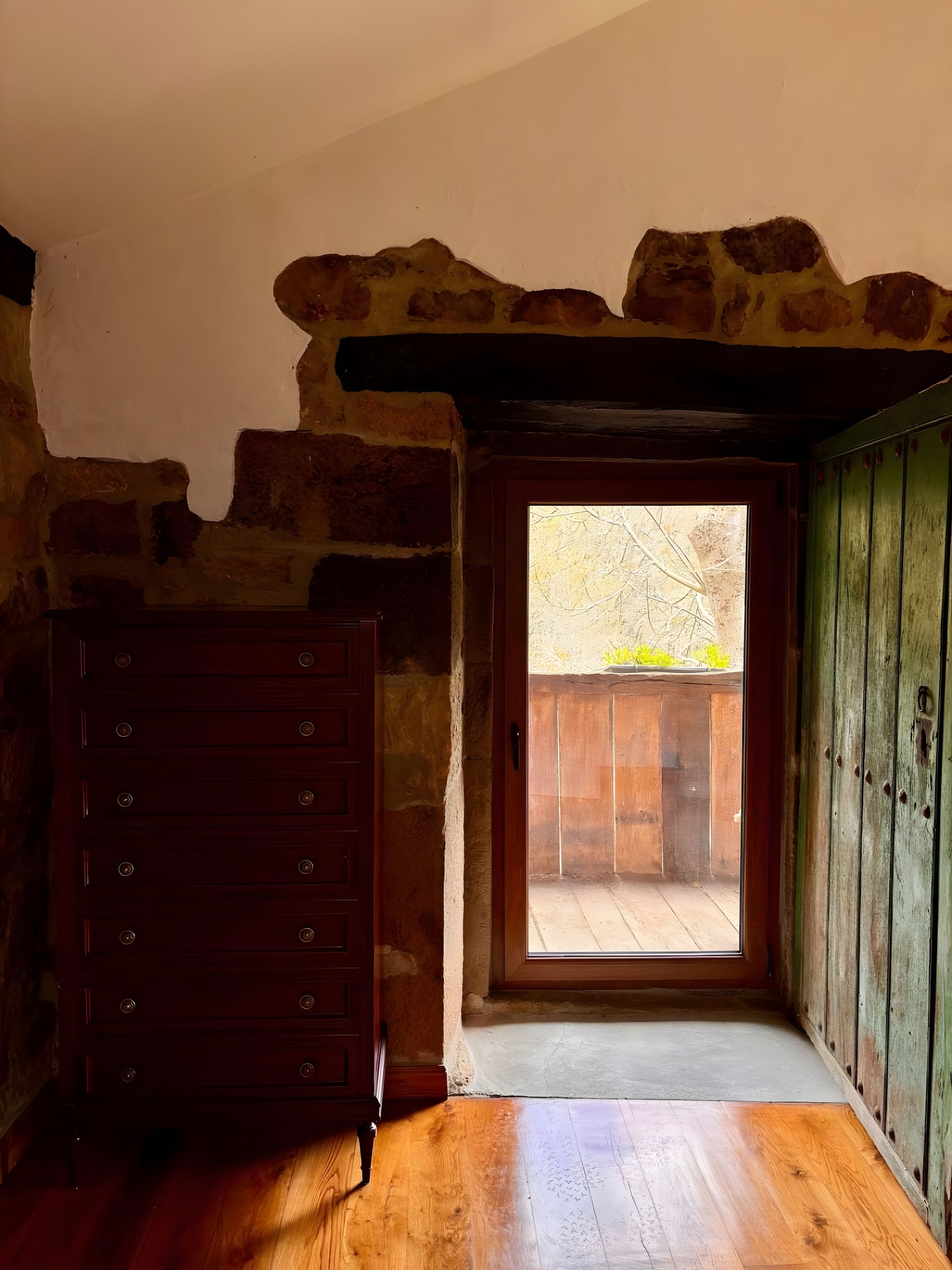 Une pièce avec une commode en bois, un mur en pierre et une porte donnant sur un espace extérieur.