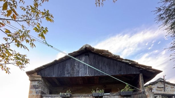 A rustic stone building with a wooden upper level, a bench outside, and a stone wall. - Lo Macario Pasiego Cabin (Resconorio)