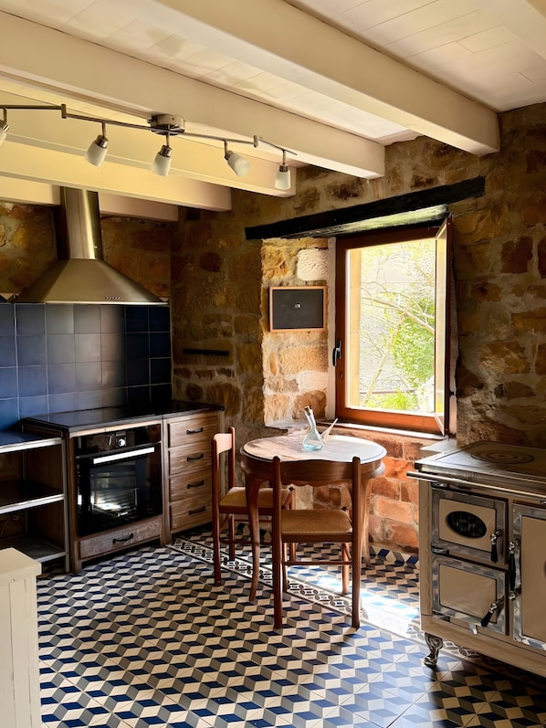 A kitchen with a stone wall, a window, a round wooden table, and a built-in oven.