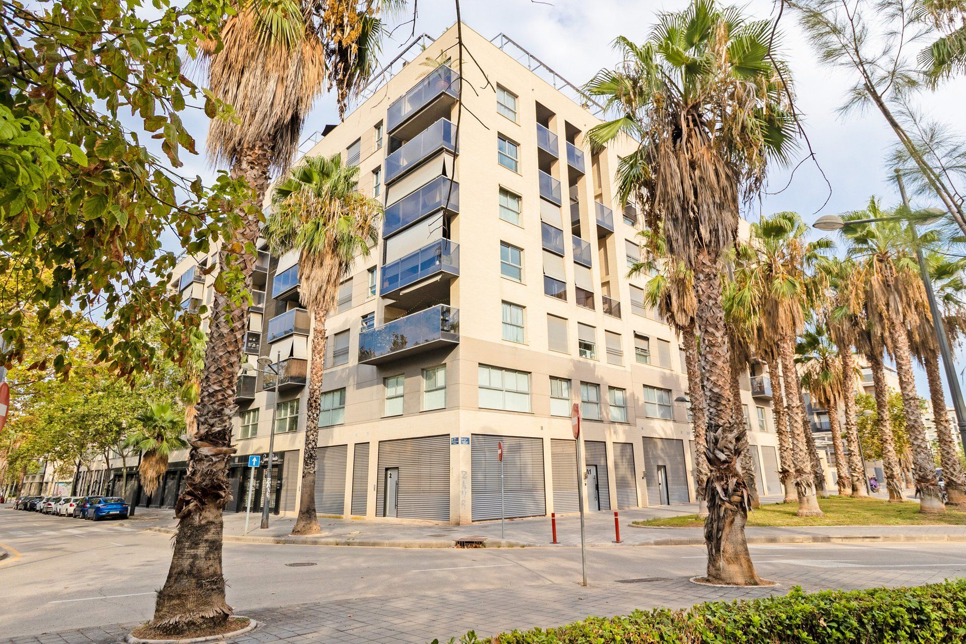 Un edificio residencial de varios pisos con balcones, rodeado de palmeras y un cielo despejado.