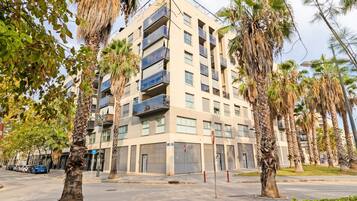 Un edificio residencial de varios pisos con balcones, rodeado de palmeras y un cielo despejado.