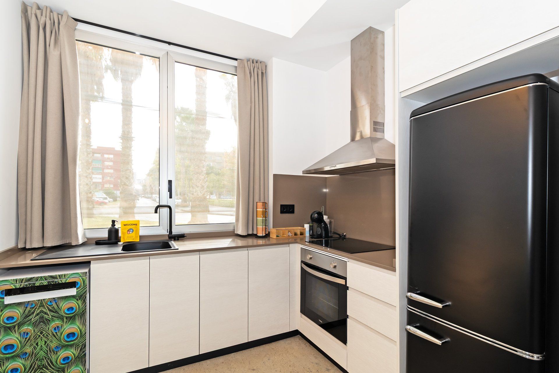 Una cocina moderna con horno integrado, un refrigerador negro y una ventana con cortinas.