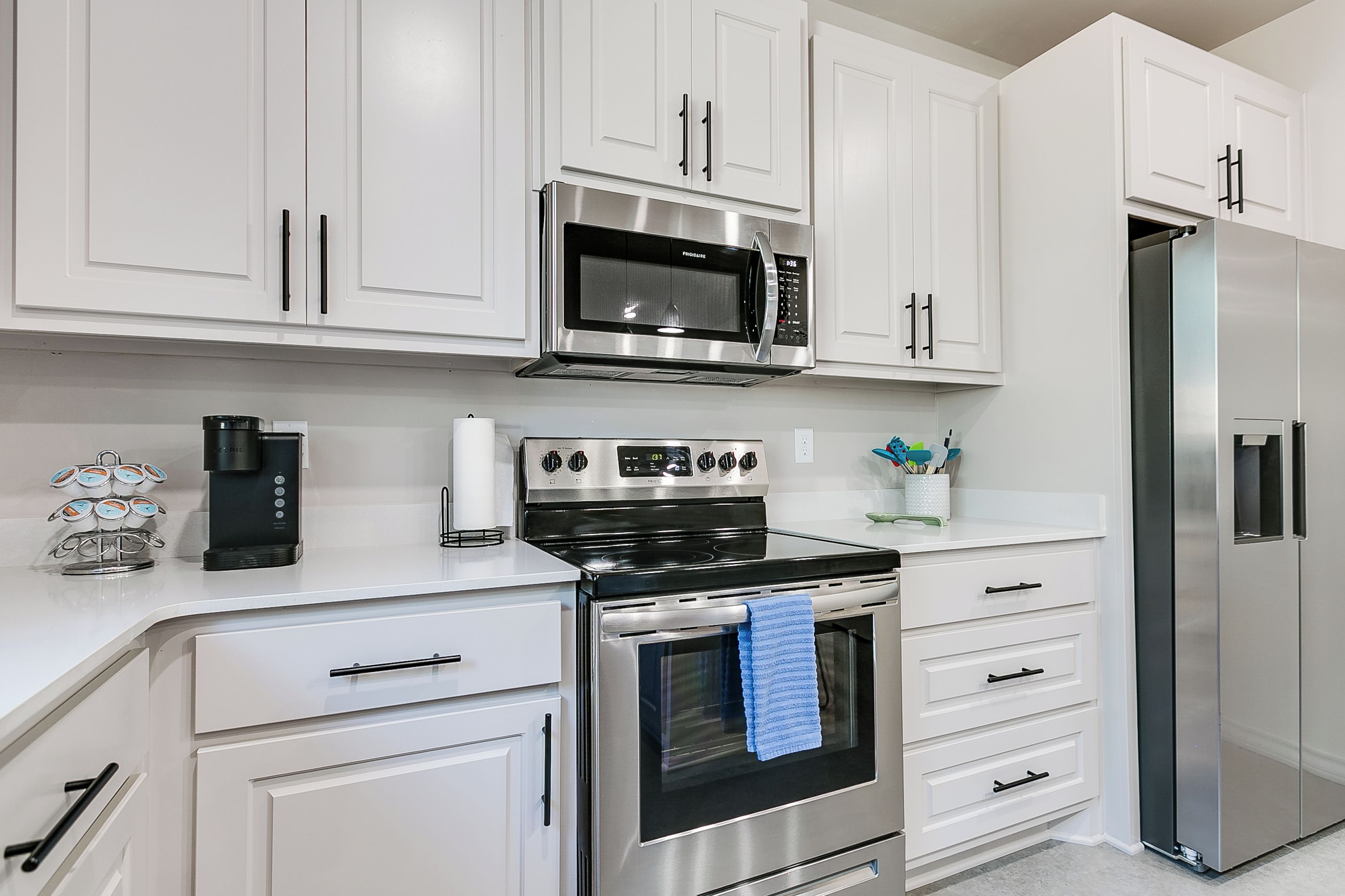 A modern kitchen with white cabinetry, a stainless steel refrigerator, a built-in oven, and a microwave.