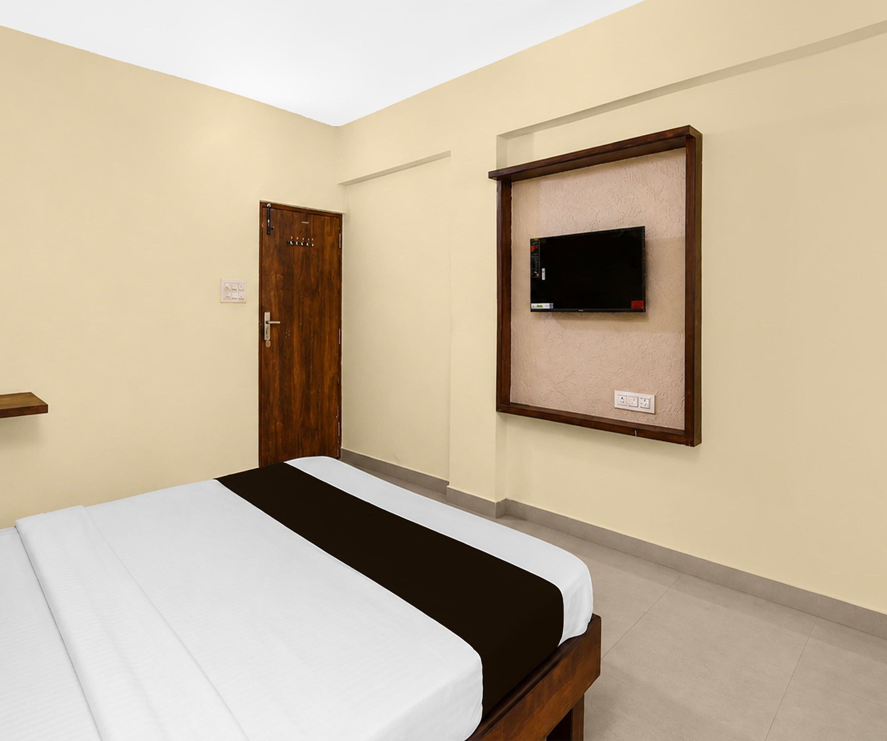 Una habitación de hotel con cama, una puerta, un televisor montado en la pared y un interruptor de luz.