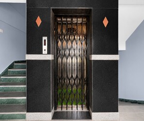 A modern elevator with a geometric metal gate, a digital display, and a staircase with green steps. - Classic Hotel Naina Luxury Rooms (Hyderabad)