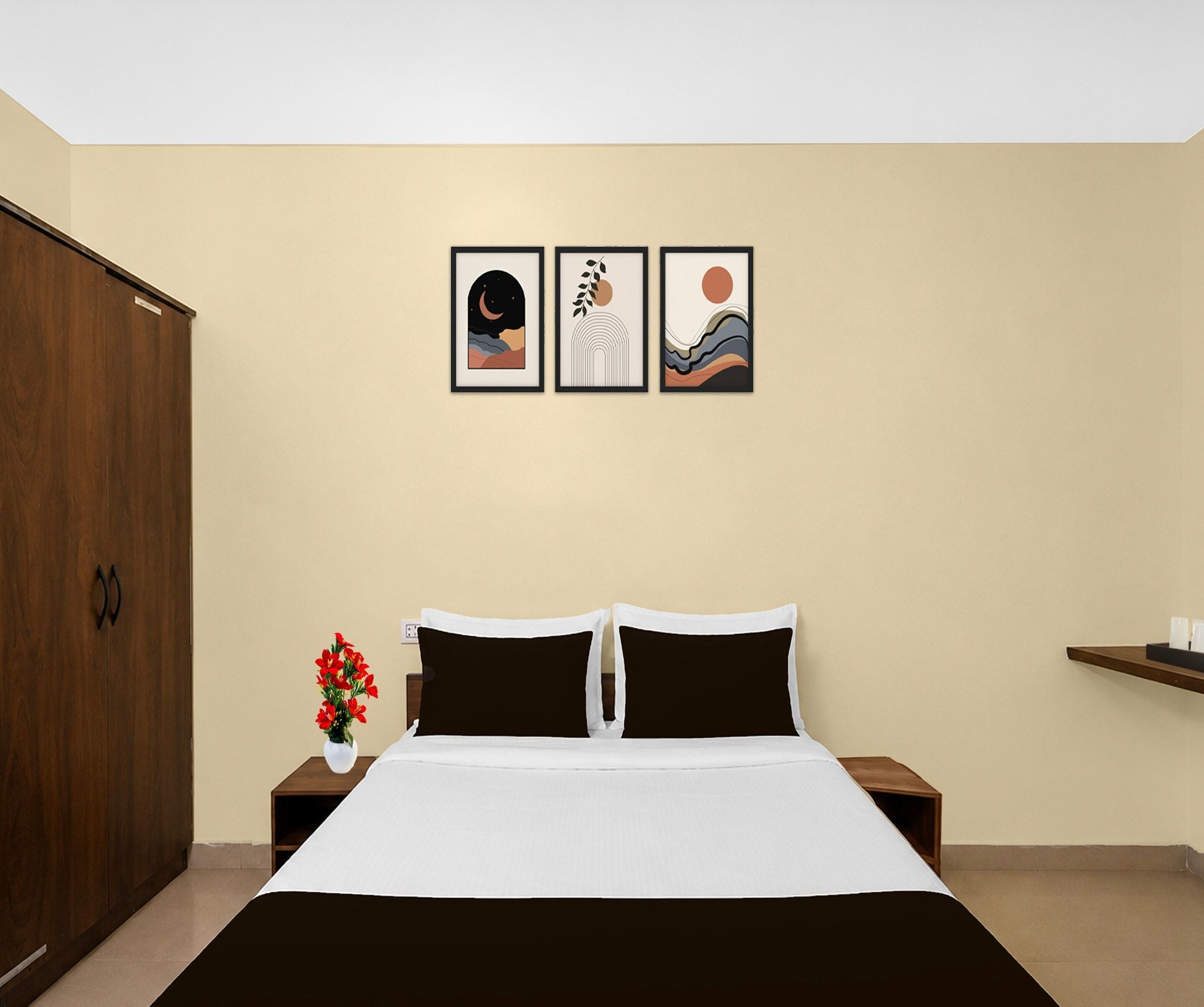 Een slaapkamer met een bed, een nachtkastje, een vaas met bloemen en drie ingekaderde foto’s aan de muur.
