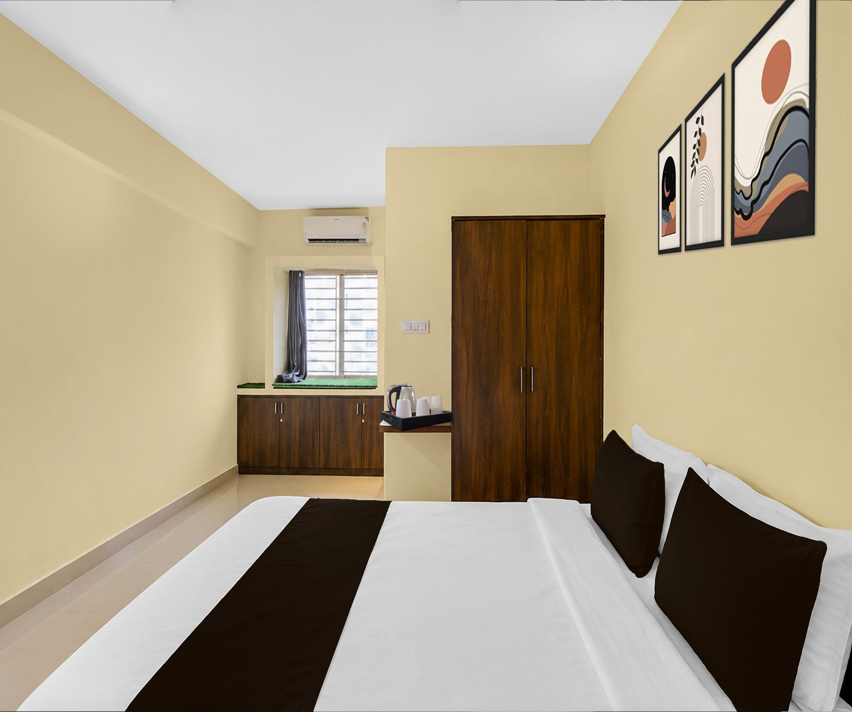A hotel room with a large bed, a wardrobe, a desk with a kettle, and artwork on the wall.