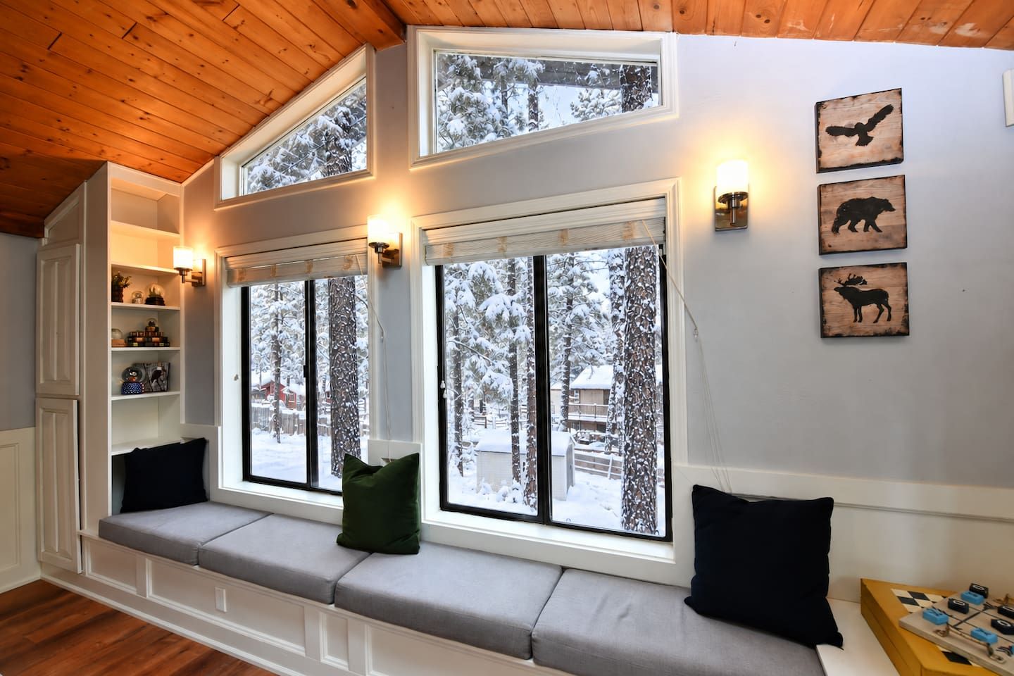 Una habitación acogedora con un banco empotrado, amplias ventanas con vistas nevadas y obras de arte colgadas en la pared.