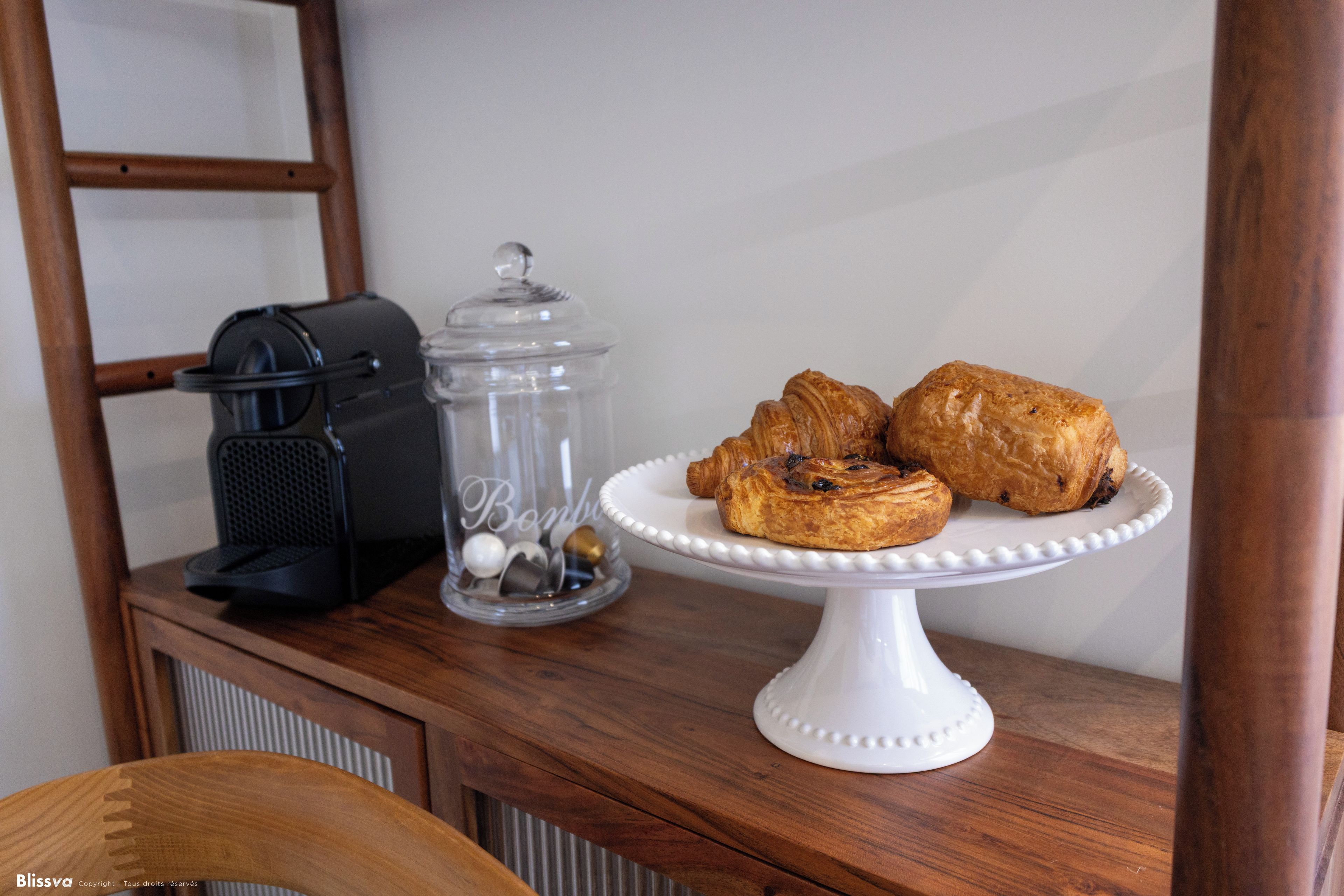 Un tavolo di legno con una macchina per il caffè, un barattolo di vetro con coperchio e un vassoio bianco con dolci.