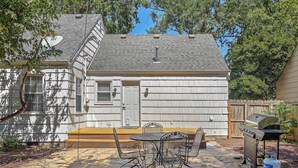 Ein Haus mit einer Terrasse, die einen Grill und Gartenmöbel bietet.
