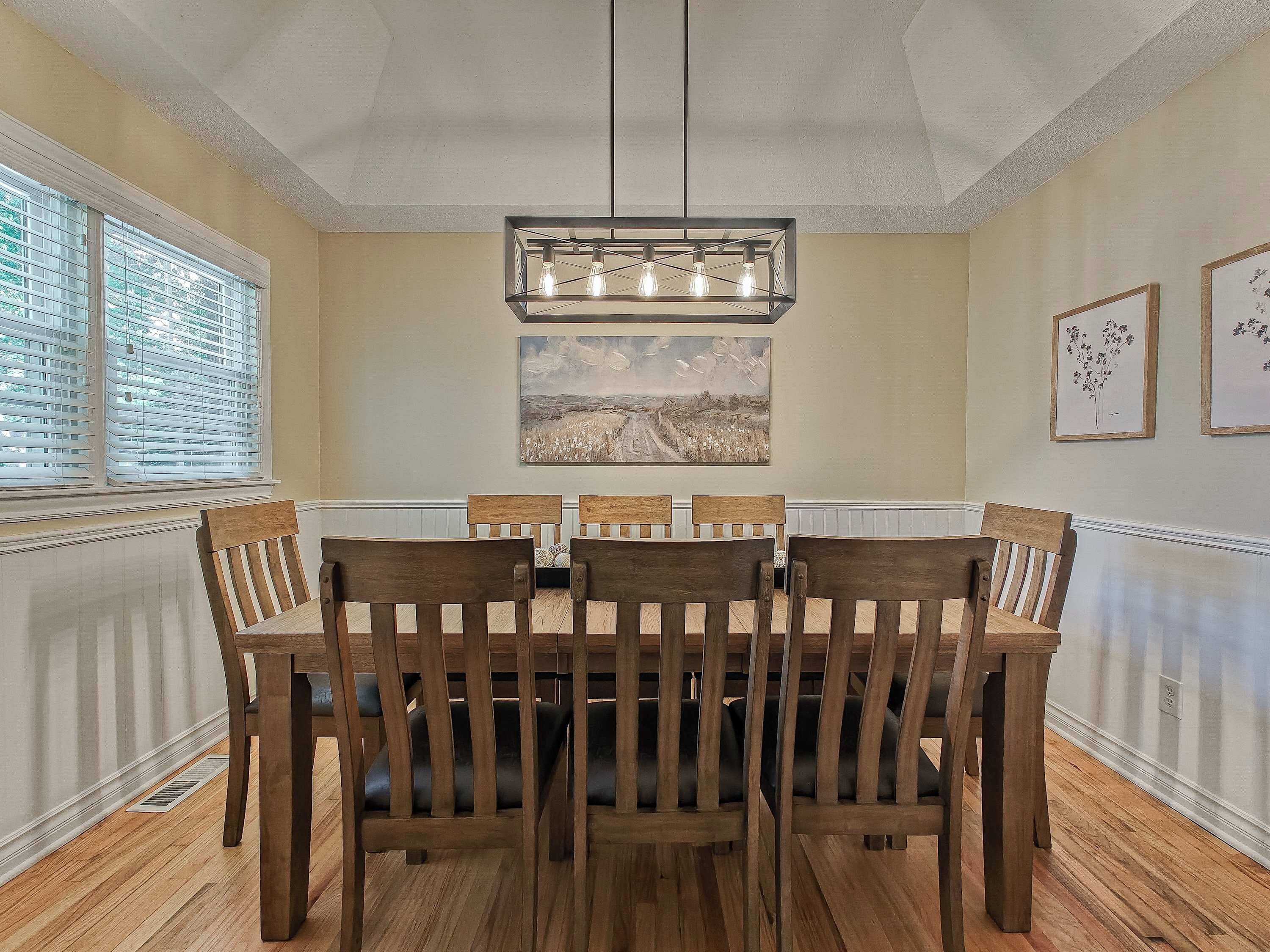 A dining room with a wooden table and chairs, a pendant light, and artwork on the walls.