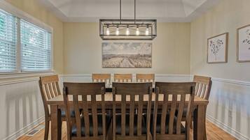 A dining room with a wooden table and chairs, a pendant light, and artwork on the walls.