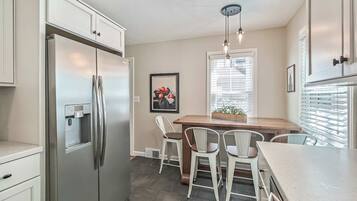 A kitchen with a stainless steel refrigerator, a built-in coffee maker, and a dining area with a wooden table and white chairs.