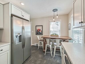 A kitchen with a stainless steel refrigerator, a built-in coffee maker, and a dining area with a wooden table and white chairs.