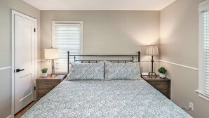 Ein Schlafzimmer mit einem Bett, zwei Nachttischen, einem Deckenventilator und einem Fenster mit Jalousien.