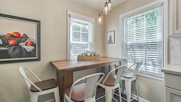 Un coin repas avec une table en bois, quatre chaises blanches, un luminaire suspendu et un tableau au mur.