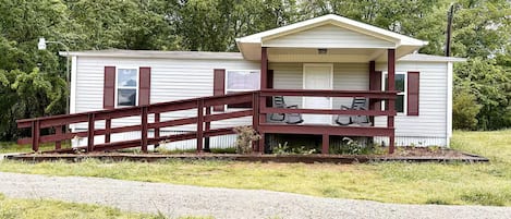 A single-story mobile home with a porch and a wooden bridge leading to the entrance.