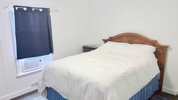 A bedroom with a bed, a window with a curtain, a nightstand, and a wooden headboard.