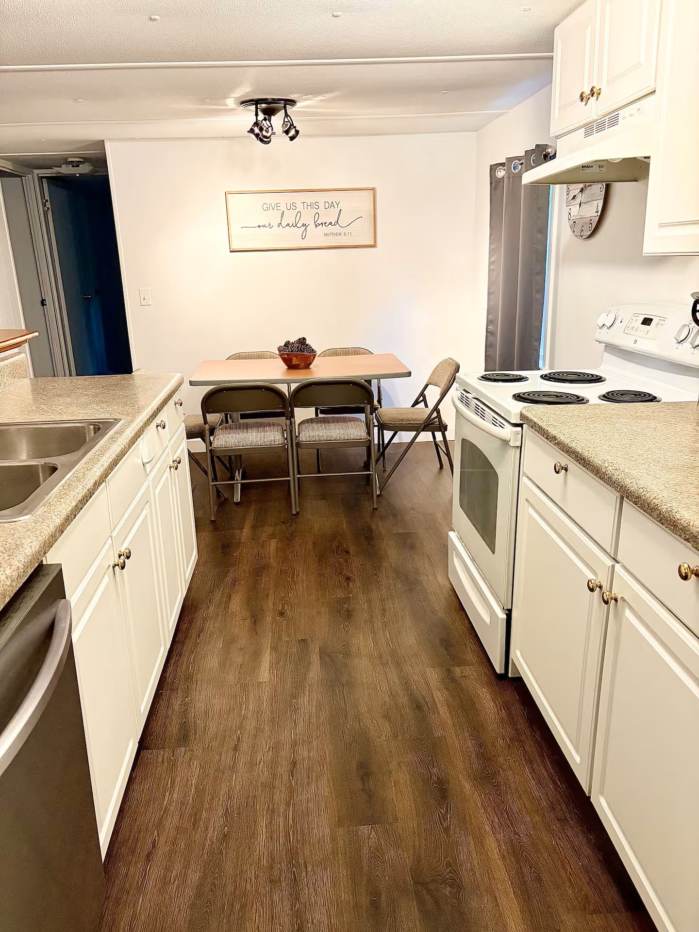 A kitchen with white cabinets, a wooden dining table with two chairs, a stove, and a clock on the wall.