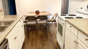 A kitchen with white cabinets, a wooden dining table with two chairs, a stove, and a clock on the wall.