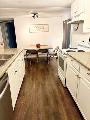 A kitchen with white cabinets, a wooden dining table with two chairs, a stove, and a clock on the wall. - Cozy Retreat - Nature Views - 5 Min to Sewanee (Sewanee)