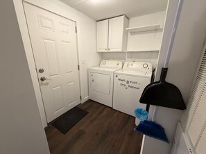 A laundry room with a washer and dryer, a door, and a small window with blinds. - Cozy Retreat - Nature Views - 5 Min to Sewanee (Sewanee)