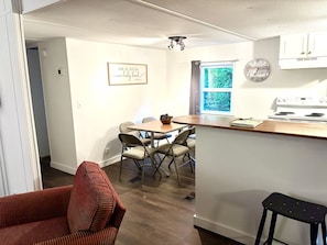 A compact kitchen with a dining area, a clock on the wall, and a window with a view of greenery. - Cozy Retreat - Nature Views - 5 Min to Sewanee (Sewanee)