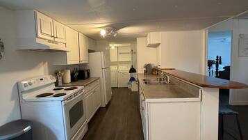 A compact kitchen with white cabinets, a stove, a refrigerator, and a sink.