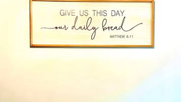 A framed inspirational quote on a wall, a wooden table with a bowl of pinecones, and a chair.