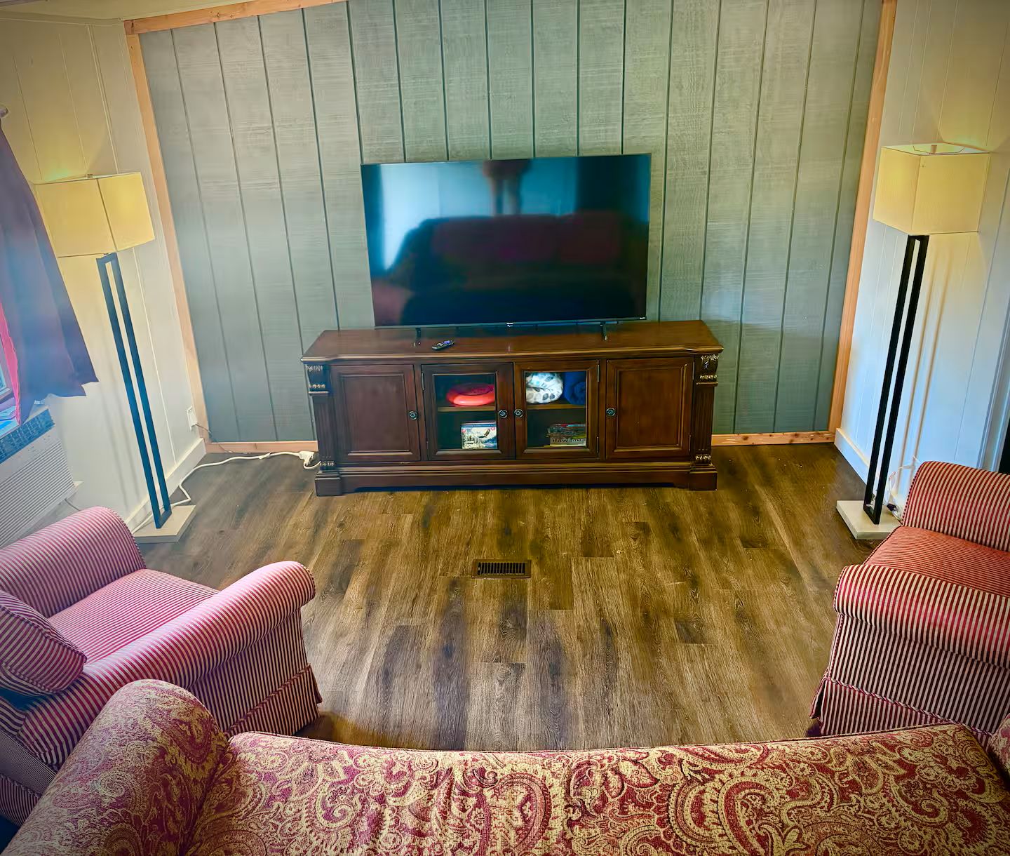 A living room with a television, a cabinet with glass doors, and striped sofas.