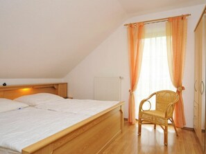 A bedroom with a wooden bed, a wicker chair, and a window with orange curtains. - 8c/t5 Holiday Home Park \"freesenbruch\" (Zingst)