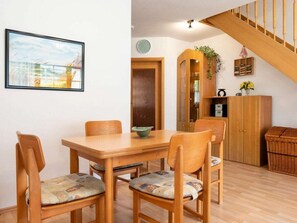 A dining area with a wooden table and chairs, a clock on the wall, and a staircase leading to an upper level. - 8c/t5 Holiday Home Park \"freesenbruch\" (Zingst)