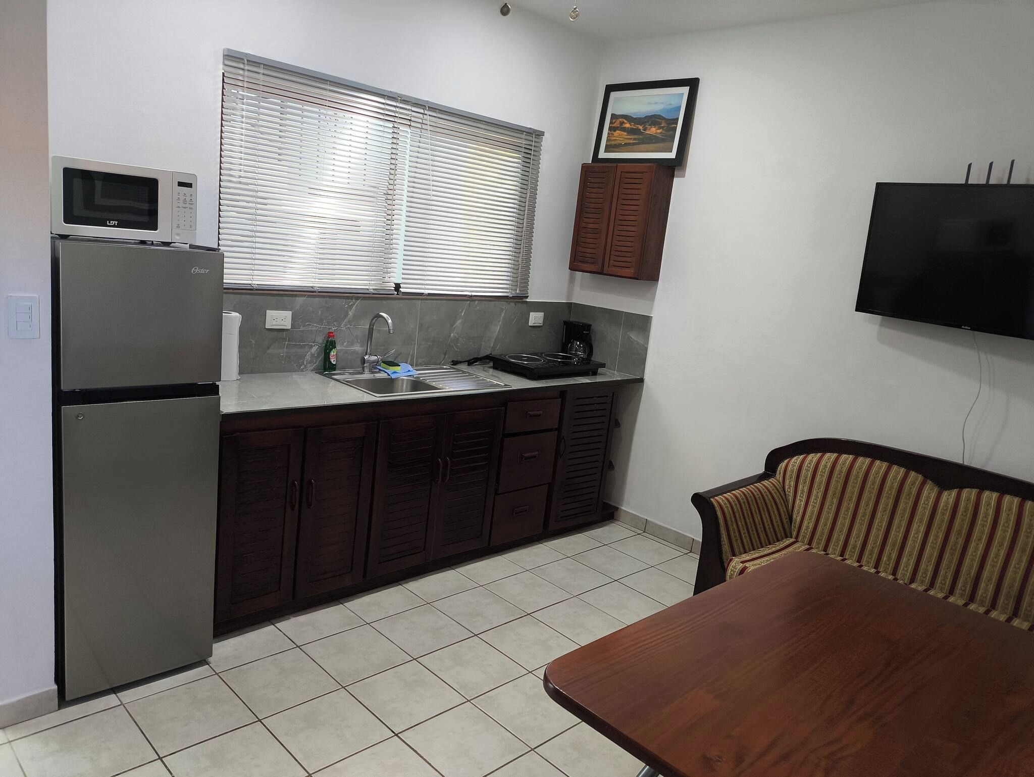 A compact kitchen with a refrigerator, microwave, sink, and stove. There is a dining table and a chair.