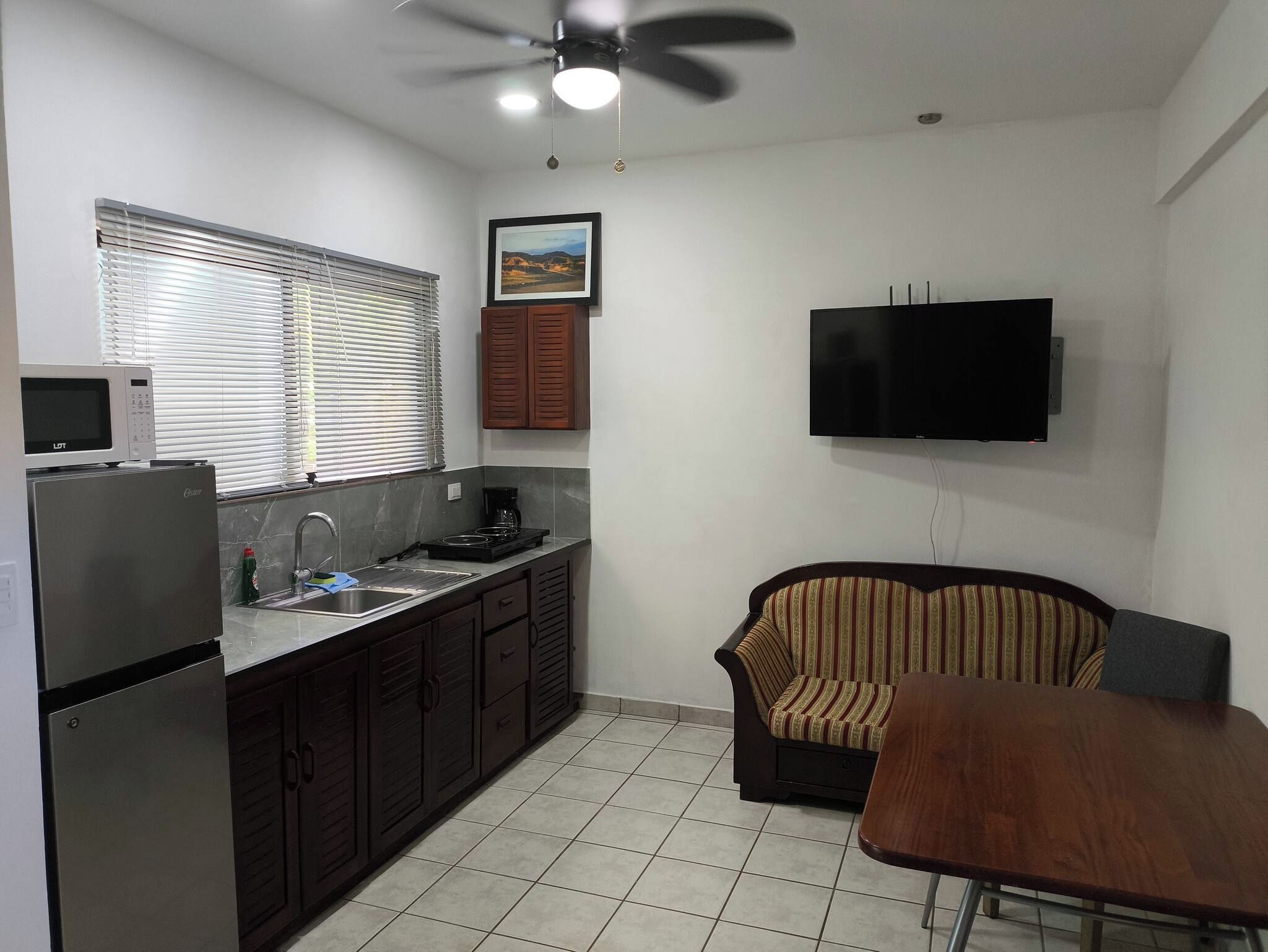 A compact kitchen with a microwave, stove, sink, and a ceiling fan.