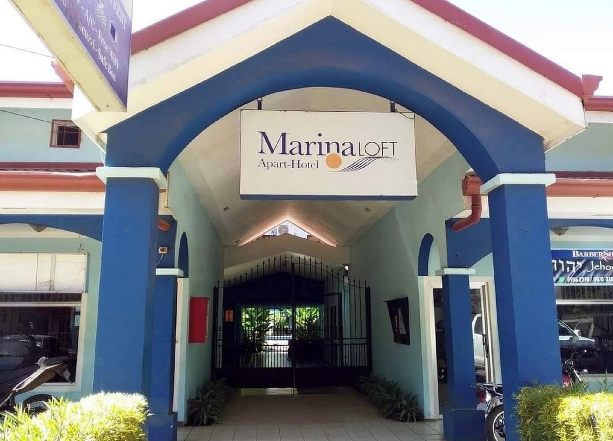 The entrance of a Marina Loft Apart-Hotel with a covered walkway and a sign above the entrance.