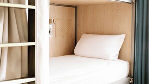 A single bed with a white mattress and pillow in a room with wooden walls and a window with curtains. - Glint Bordeaux (Bordeaux)