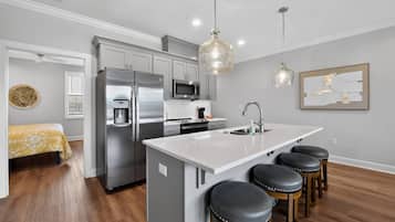 A modern kitchen with stainless steel appliances, a central island with stools, and pendant lighting.