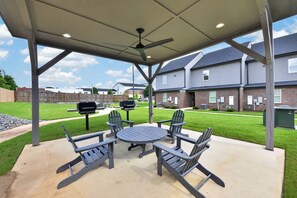 Patio esterno con tavolo e sedie, una ventola a soffitto e vista su edifici residenziali.